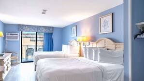Ett hotellrum med två sängar, ett skrivbord, en stol och en balkong med blå gardiner.
