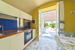 A compact kitchen with a gas stove, oven, and sink, leading to a patio with outdoor seating. - Cobalt (Barano D'ischia)