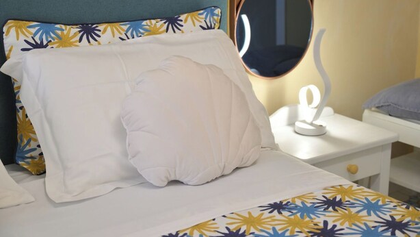 Un llit amb un coixí blanc i un coixí decoratiu, una taula de nit amb un mirall i una petita làmpada.