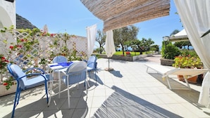 Terrassa exterior amb taula i cadires, envoltada de plantes en testos i vista al mar.