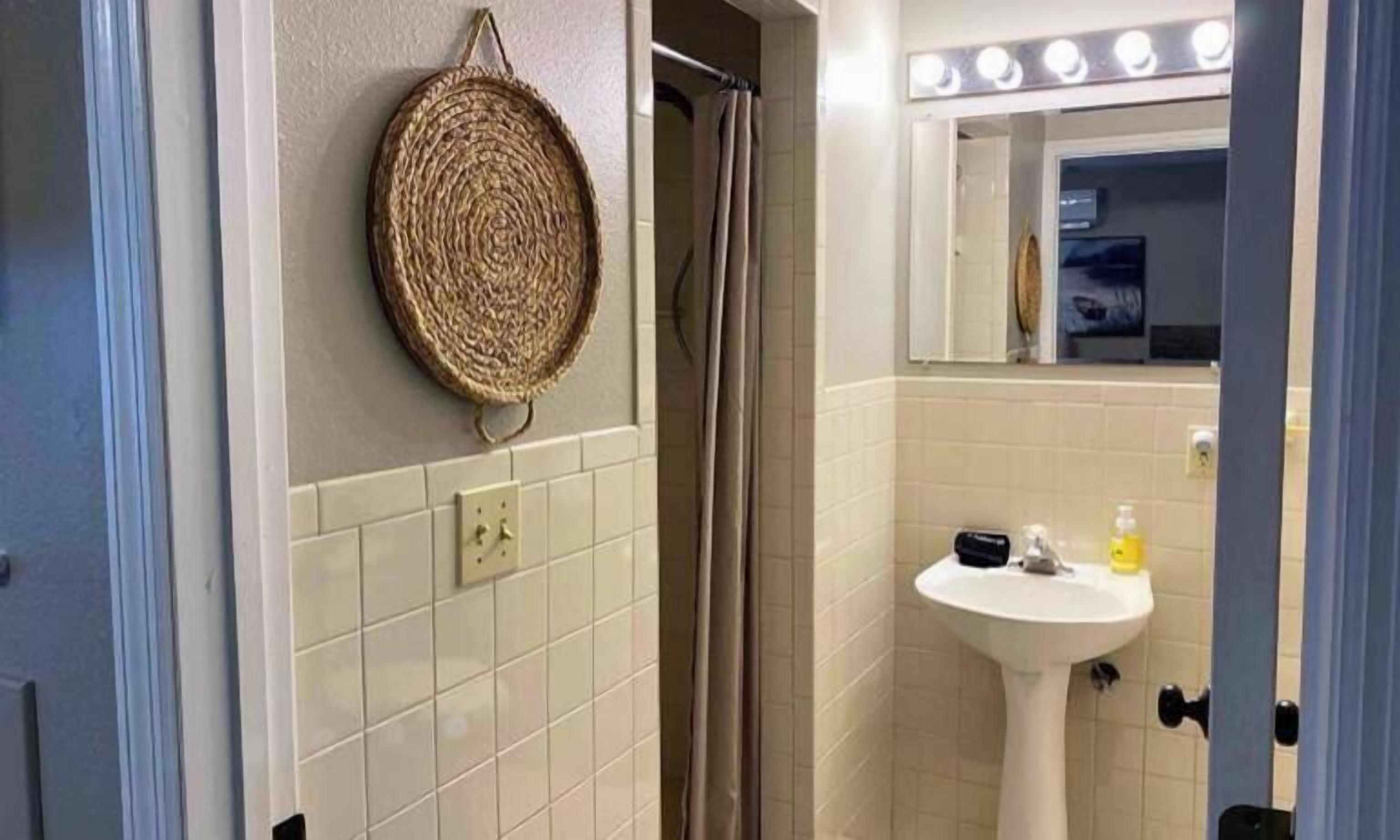 A bathroom with a sink, mirror, and a woven mat on the wall.