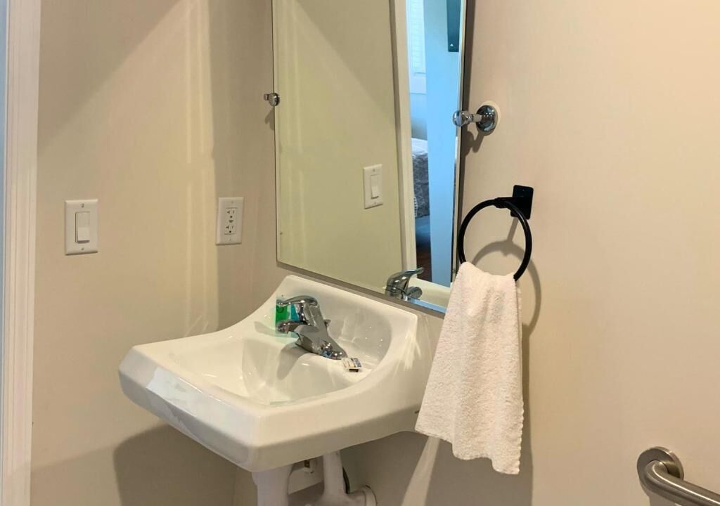 Une salle de bain avec un lavabo blanc, un miroir, un porte-serviettes et une porte visible donnant sur une autre pièce.