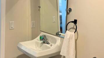 Une salle de bain avec un lavabo blanc, un miroir, un porte-serviettes et une porte visible donnant sur une autre pièce.