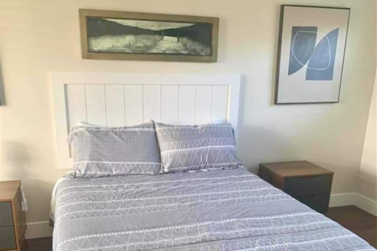 A bedroom with a bed, a nightstand, a framed picture above the bed, and a framed abstract art piece on the wall.