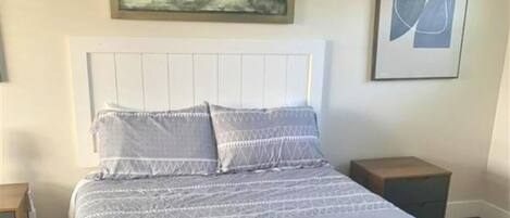 Un dormitorio con cama, un mesita de noche, un cuadro enmarcado sobre la cama y una obra de arte abstracta en la pared.