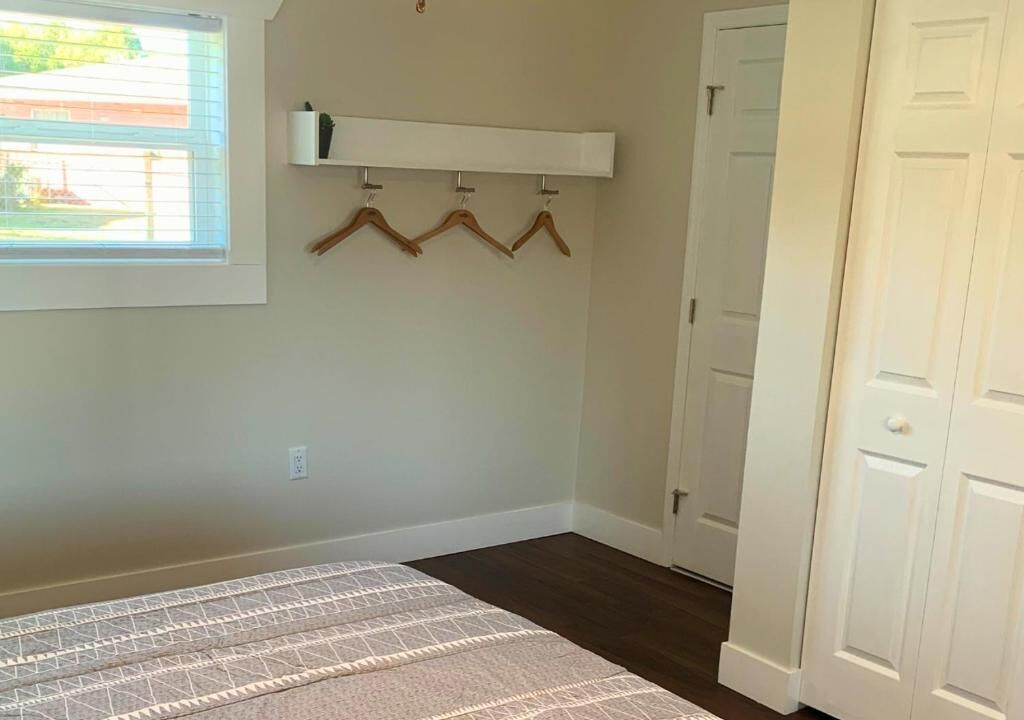 Um quarto com uma cama, uma janela, uma prateleira na parede e uma porta.