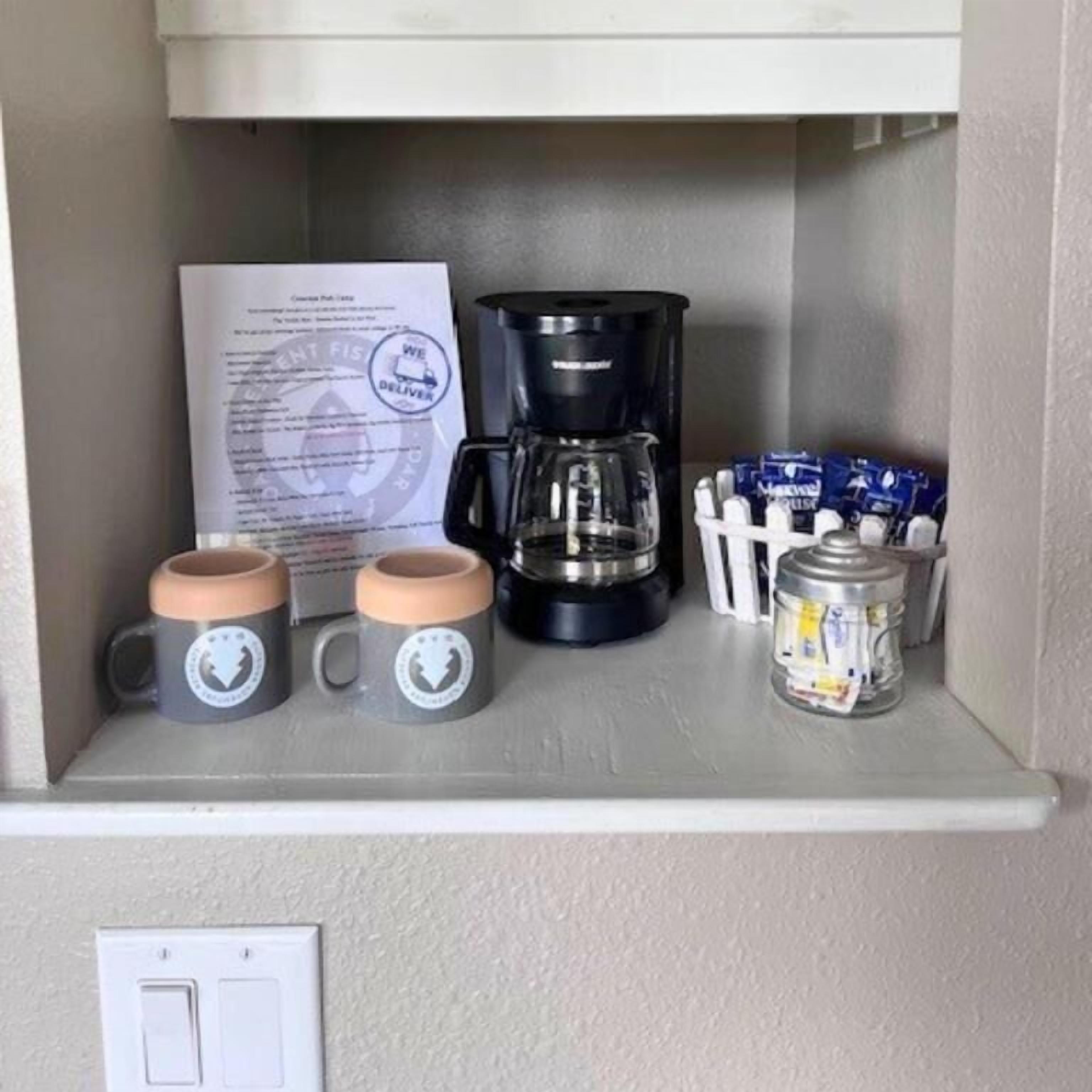 Una kitchenette con cafetera, dos tazas, un tarro y un menú.
