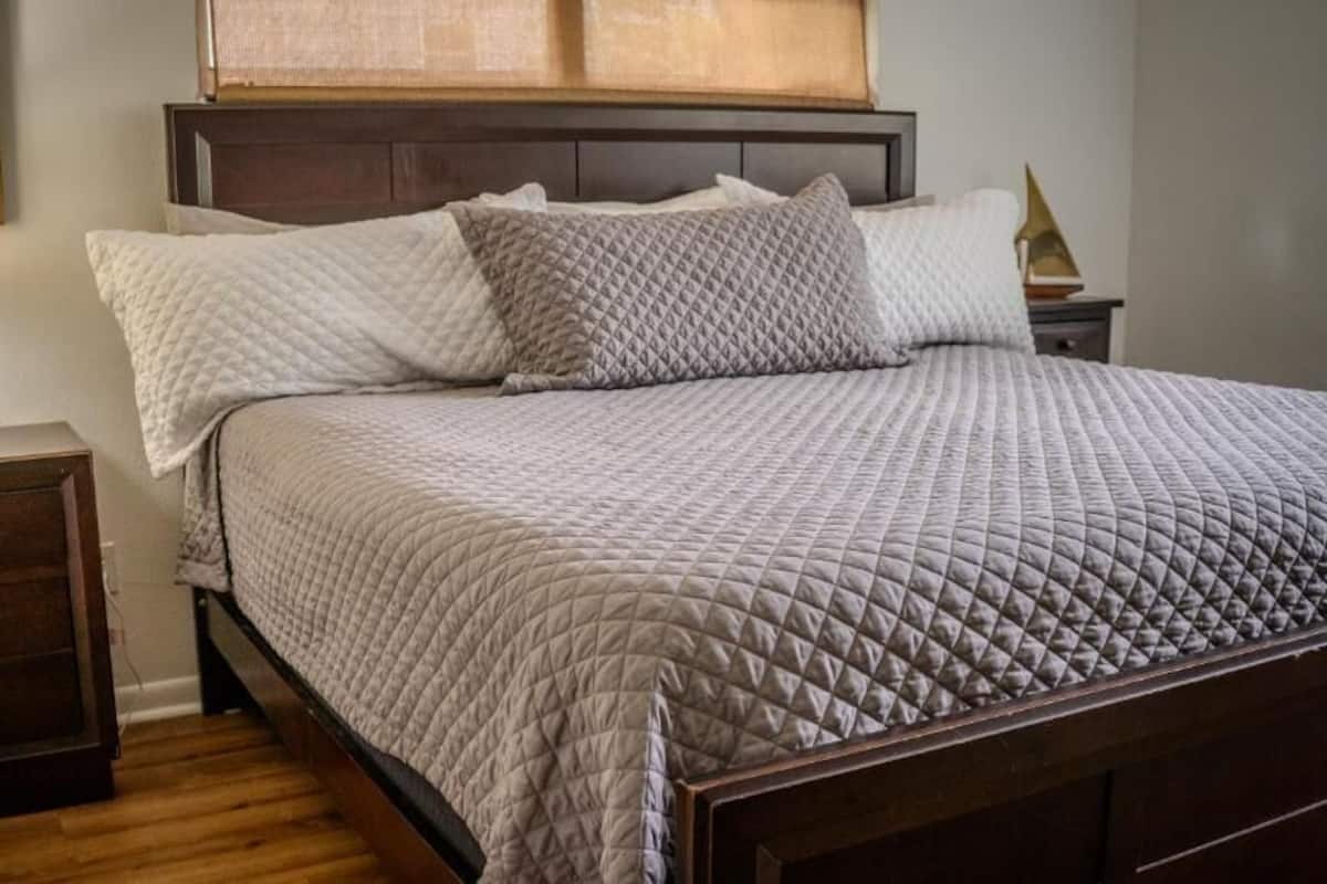 A neatly made bed with a quilted cover, a bedside lamp, and a nightstand with drawers.