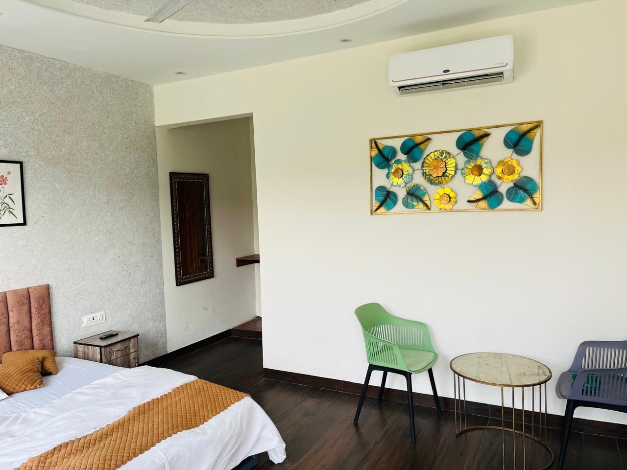 A hotel room with a bed, a small table, two chairs, an air conditioning unit, and a decorative wall piece.