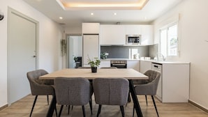 Une cuisine moderne avec des meubles blancs, un îlot central et un coin repas doté de chaises grises.