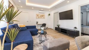 Un salon moderne avec un canapé d’angle, une table basse, un pouf gris, un téléviseur et une œuvre d’art représentant une carte du monde accrochée au mur.