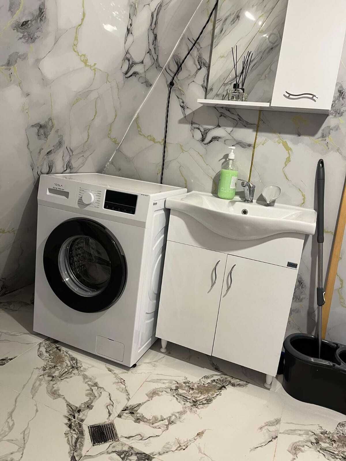 A compact laundry area with a washing machine, a sink, and a mop.
