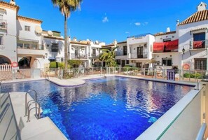 A swimming pool surrounded by white buildings with balconies, clear skies, and a palm tree. - Beautiful Andalusian Casa in stunning Nerja a short walk to Burriana and town (Nerja)