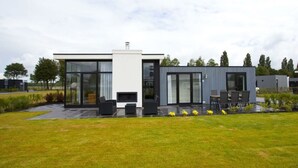Ett modernt hus med stora fönster, en uteplats med utemöbler och en välskött gräsmatta.