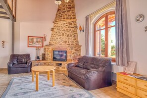A living room with a stone fireplace, leather sofas, a wooden coffee table, and a television. - Lithos - Stay Lithos (Leonidion)