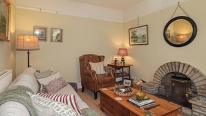 Ein Wohnzimmer mit Sofa, Sessel, Couchtisch, Kamin und Wandlampen.