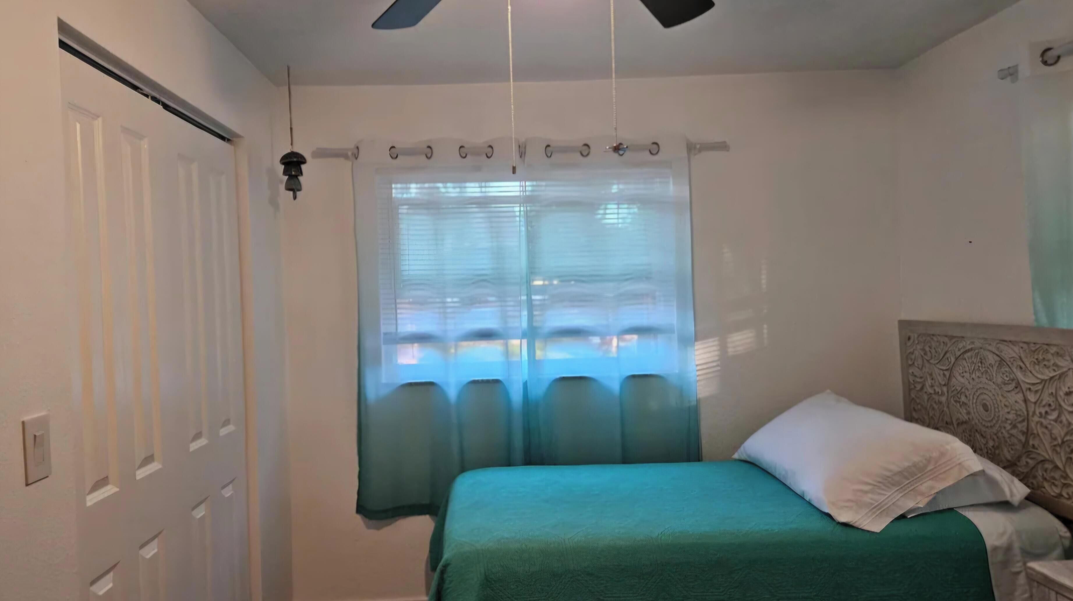 Un dormitorio con cama, cortinas, ventilador de techo y ventana con persianas.