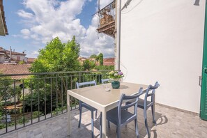 Un balcón con una mesa y sillas, una planta en maceta y vistas a edificios y áreas verdes.