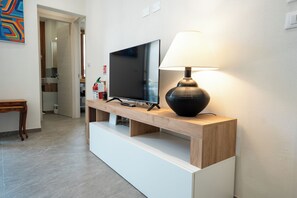 Una sala de estar moderna con un televisor de pantalla plana sobre un mueble de madera, una lámpara negra y un banco de madera.