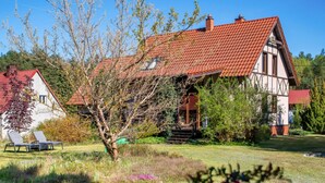 A traditional half-timbered house with a red-tiled roof, a lawn with a dog, and a clear blue sky.