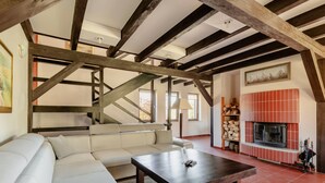 A living room with a white sofa, a wooden coffee table, exposed wooden beams, a fireplace, and a staircase.
