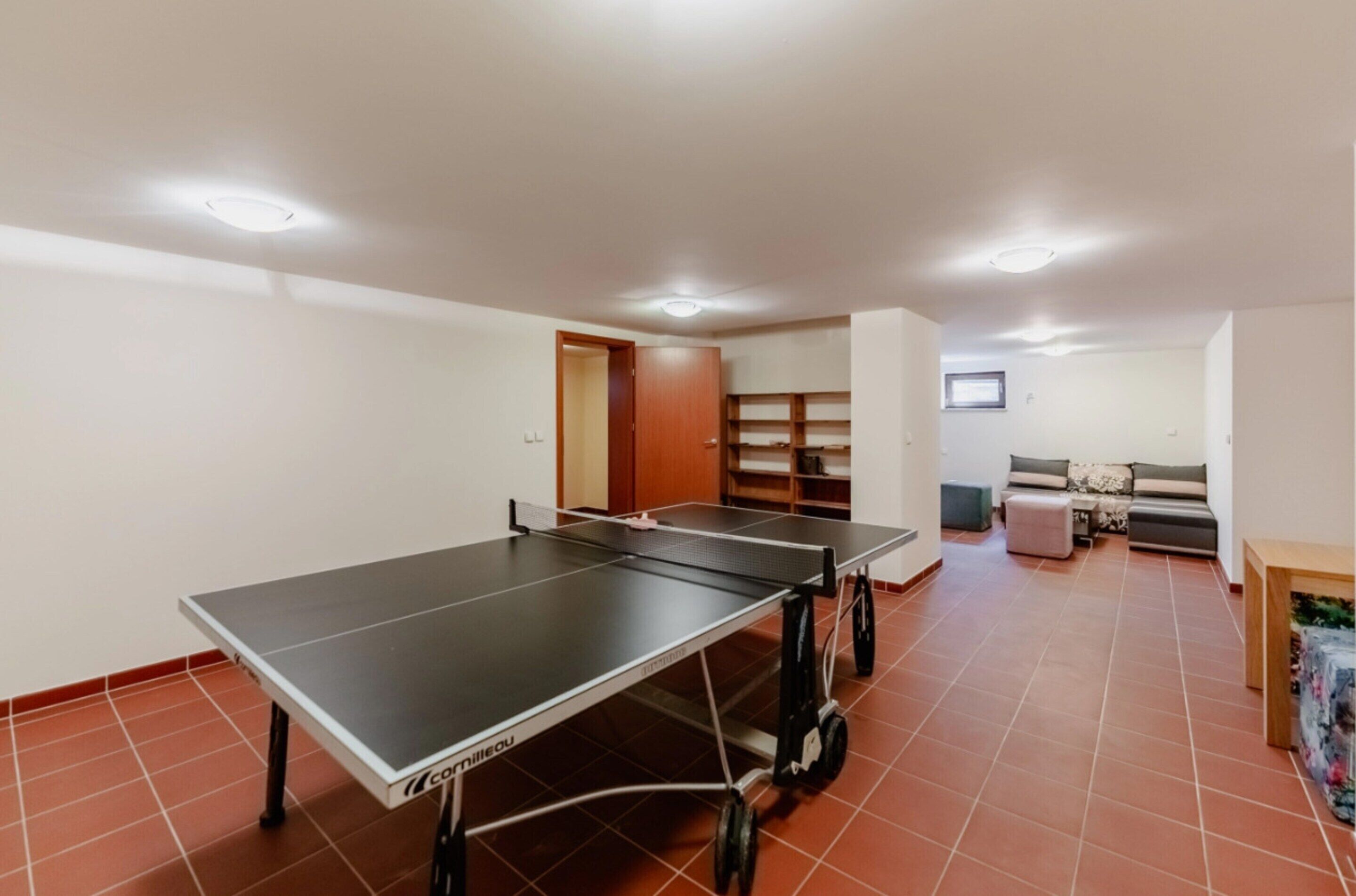 A room with a ping pong table, a sofa, a TV, and a door leading to another room.