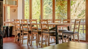 A dining area with wooden chairs and tables, large windows, and a view of trees.