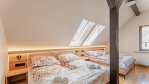 A bedroom with two beds, skylights, wooden flooring, and bedside tables.