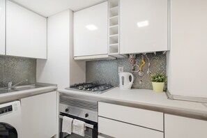 Une cuisine moderne avec des meubles blancs, une cuisinière à gaz, une bouilloire et un dosseret carrelé.