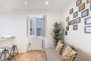 A modern living room with a sofa, a dining area with stools, a large window, and a wall decorated with framed pictures. - Rossio Boutique Apartment 2 (Lisbon)