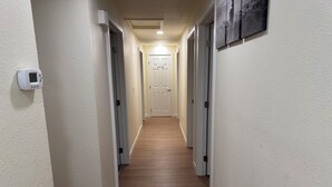 Um corredor com piso de madeira, paredes brancas e uma porta no final.