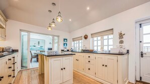A spacious kitchen with white cabinetry, a central island, pendant lighting, and a view of the dining area through an open door. - Stunning Emsworth Family Home - Pass the Keys (Emsworth)