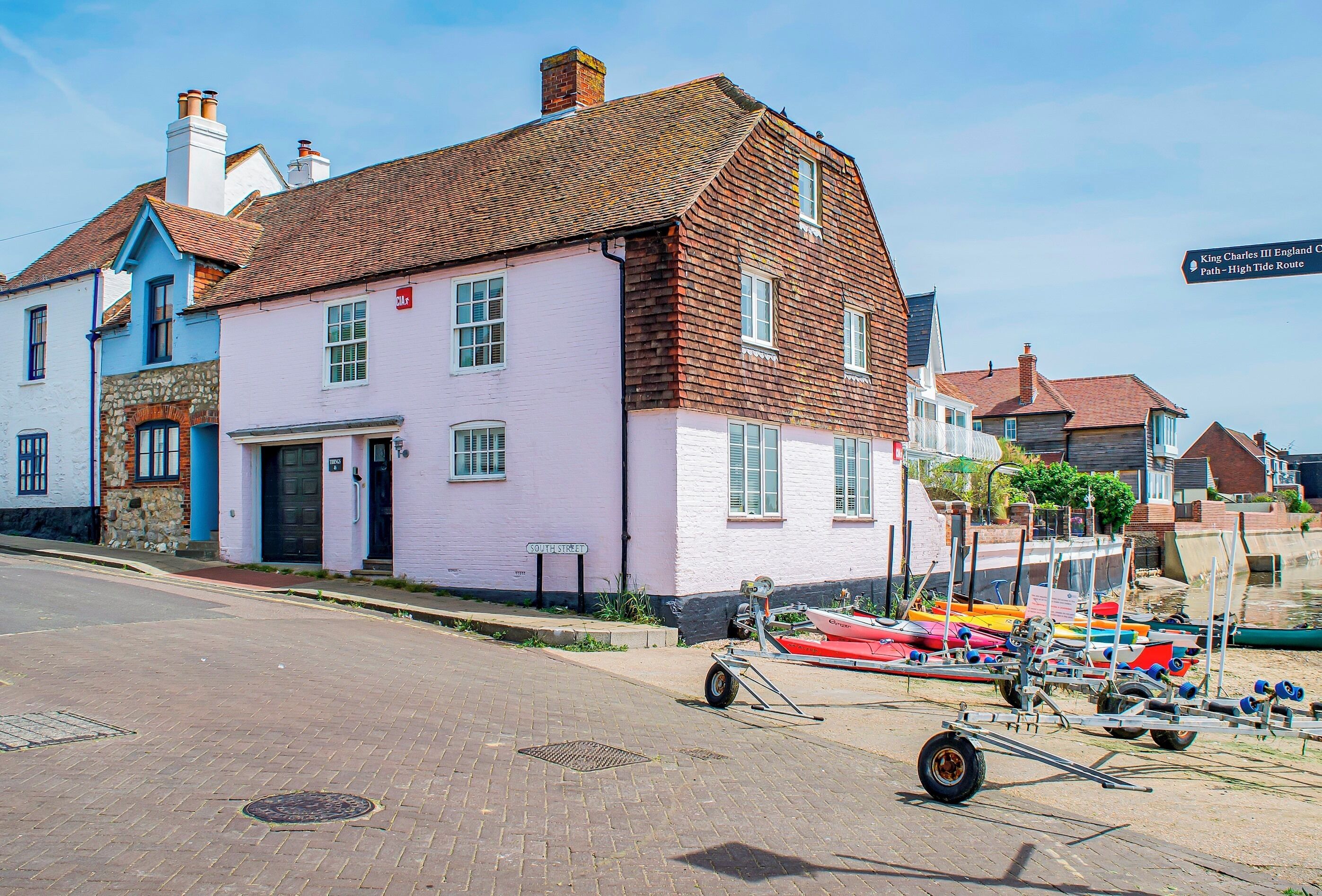 A building with a red roof and white walls, a street in front, and boats docked by the water.