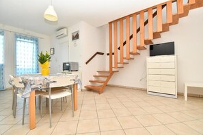 A modern living room with a wooden staircase, a dining area with a table and chairs, a TV, and a white cabinet. - Residenz Arcobaleno Two-Room Apartment Cavalluccio Marino for 6 People (Chioggia)