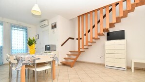 Una sala moderna con una escalera de madera, un comedor con una mesa y sillas, un televisor y un armario blanco.