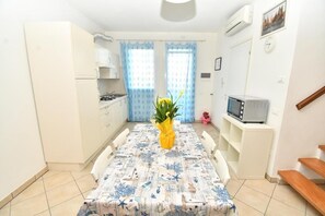 A compact kitchen with white cabinets, a dining table with a patterned tablecloth, a small TV on a stand, and a potted plant. - Residenz Arcobaleno Two-Room Apartment Cavalluccio Marino for 6 People (Chioggia)