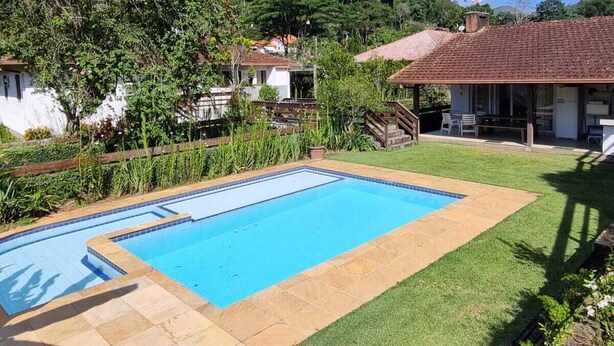 Una piscina rectangular con solárium empinado, rodeada por un césped y una colina al fondo.