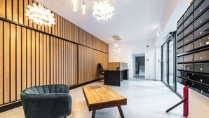 A modern lobby with a wooden wall, a reception desk, a blue chair, a wooden table, and a storage unit with drawers. - Urban Amethyst Haven - 1BR Apartment with Balcony (București)