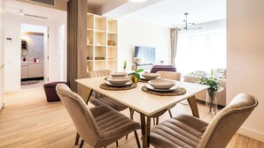 A modern dining area with a wooden table, cushioned chairs, and a pendant light. - Urban Amethyst Haven - 1BR Apartment with Balcony (București)