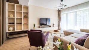 A modern living room with a sofa, a purple chair, a television, and a bookshelf. - Urban Amethyst Haven - 1BR Apartment with Balcony (București)