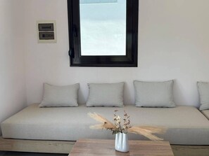A room with a sofa, a window, and a vase with dried plants.