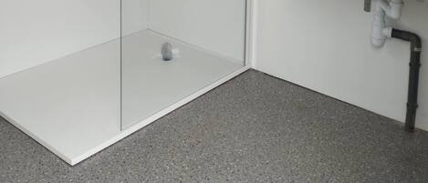 A shower with a glass door, a sink with a mirror, and a bottle of cleaning product on the counter.