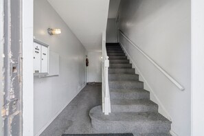 A staircase with a handrail, carpeted steps, and a wall-mounted mailbox. - Winrock Apartments by Andes STR (Houston)