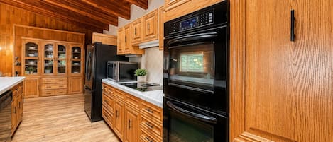 Une cuisine avec des meubles de rangement en bois, un réfrigérateur noir, un four à micro-ondes et un four traditionnel.