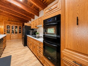 A kitchen with wooden cabinets, a black refrigerator, a microwave, and an oven. - Family-Friendly Cabin with Filtered Lake Views, Bunk Rooms, Game Space & Deck. (Cascade)
