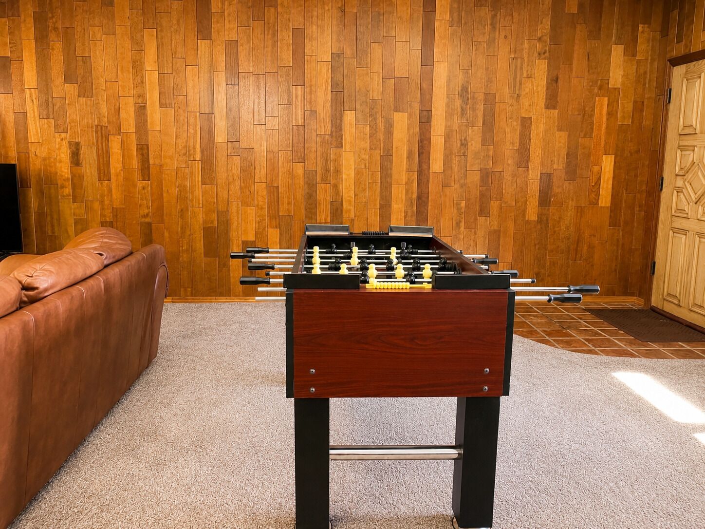 Una habitación con piso de parquet de madera, un sofá de cuero marrón y una mesa de futbolín.