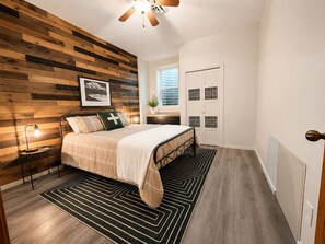 A bedroom with a bed, a wooden wall panel, a ceiling fan, a window, and a door. - Family-Friendly Cabin with Filtered Lake Views, Bunk Rooms, Game Space & Deck. (Cascade)