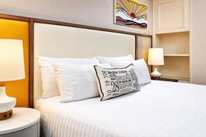 Ein Hotelzimmer mit einem Bett, zwei Kissen, einem Nachttisch mit Lampe und einem an der Wand hängenden Kunstwerk.