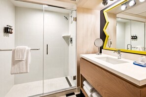 Ein modernes Badezimmer mit Duschkabine aus Glas, einem weißen Waschbecken mit Spiegel und einer Holz-Kommode.
