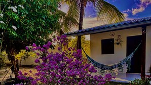 A house with a hammock, a small garden with purple flowers, and a palm tree. - House on the River (Barra do Jacuipe)